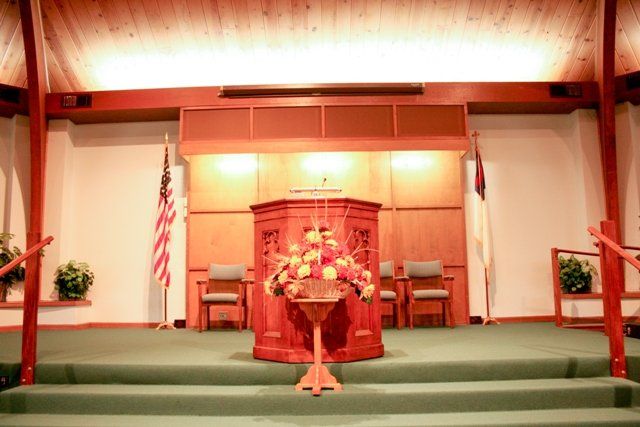 Interior view of a church with a central pulpit, flowers, and flags displayed on either side.