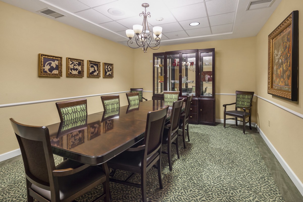 A well-furnished dining or conference room featuring a large wooden table surrounded by chairs, with artwork on the walls and a chandelier overhead.