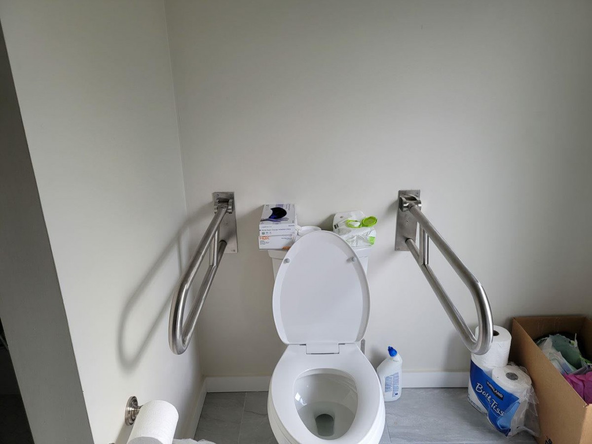 An accessible bathroom featuring a toilet with support handrails and hygiene products.