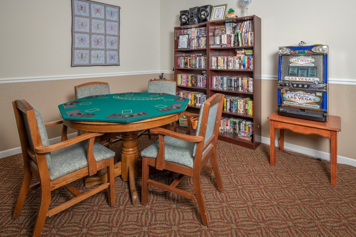 A cozy game room featuring a poker table with chairs, a bookshelf filled with books, and a slot machine.
