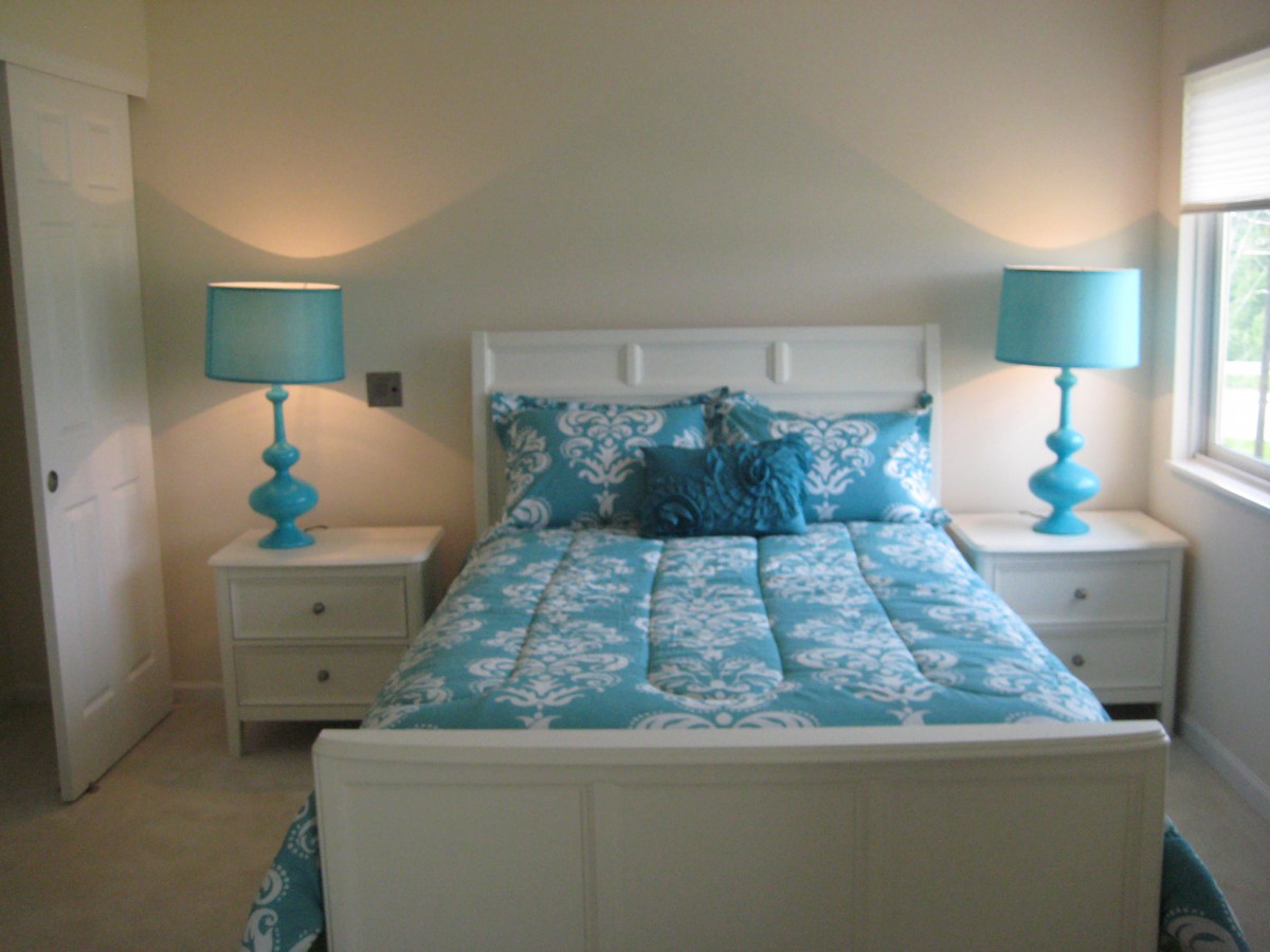 A stylish bedroom featuring a bed with turquoise bedding and matching lamps.