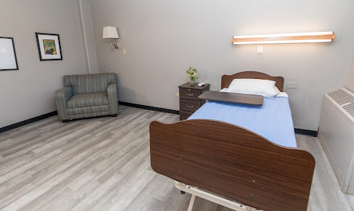 A serene hospital room featuring a wooden bed with blue bedding, a small bedside table, and a comfortable sofa.