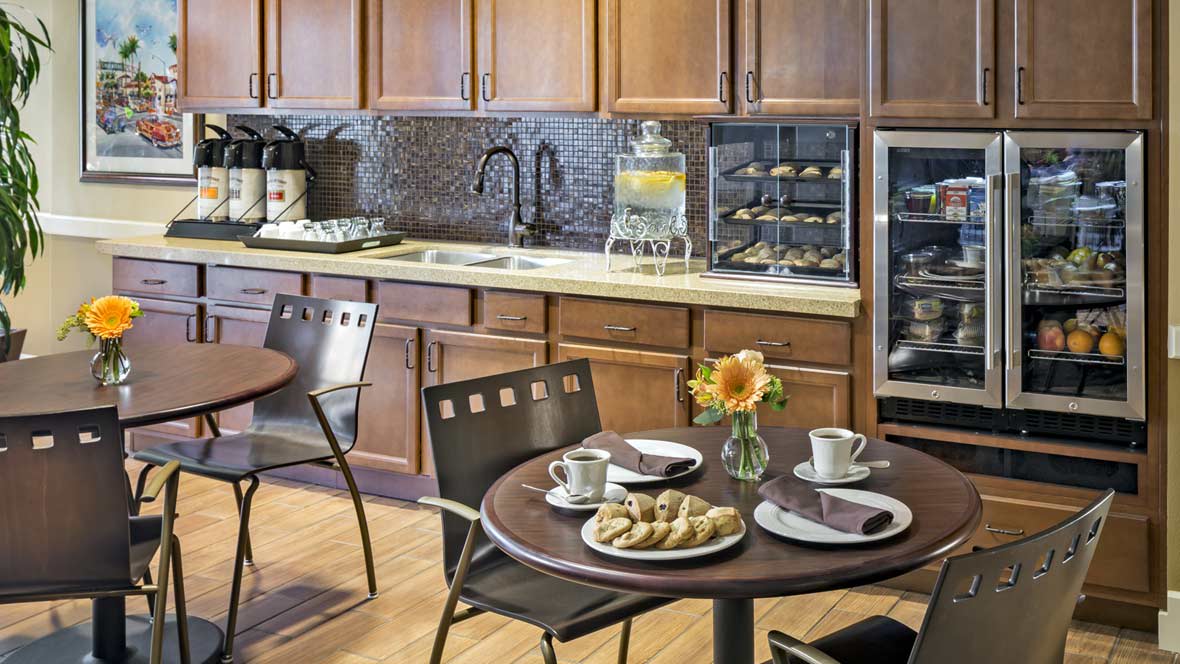 A cozy kitchen and dining area featuring a table set with cookies, coffee cups, and a small flower vase.
