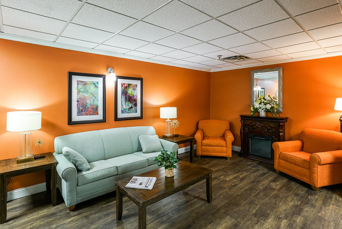 A cozy living room with bright orange walls, featuring a light green sofa, two orange armchairs, a wooden coffee table, and decorative artwork.