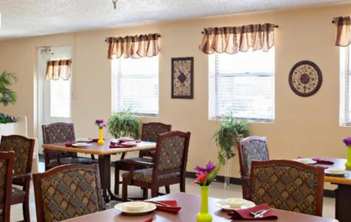 A well-lit dining area with neatly arranged tables and chairs, complemented by decorative plants and window treatments.