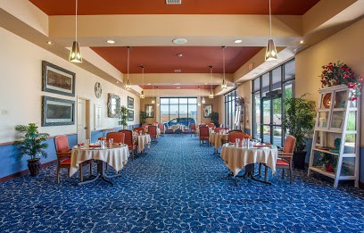 A spacious restaurant interior with neatly arranged tables and chairs, decorated with elegant lighting and large windows.