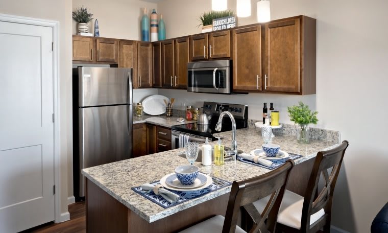 A modern kitchen with stainless steel appliances and a granite countertop, featuring a small dining setup.