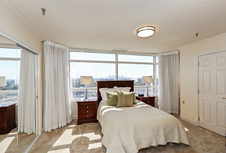A bright and spacious bedroom with a large window, featuring a neatly made bed and matching nightstands with lamps.