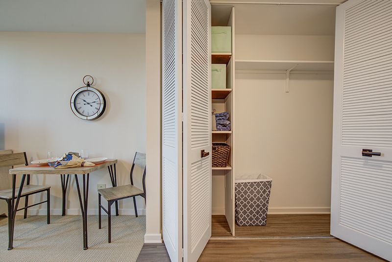 A neatly organized closet and dining area with shelves, a table, chairs, and a wall clock.