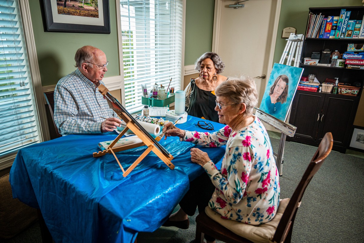 Elderly individuals participate in an art class, painting together at a table.