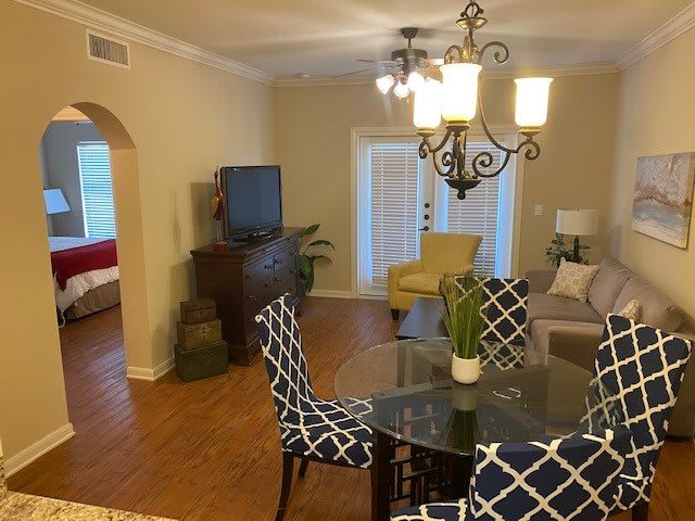 A cozy living and dining area with a mix of modern and classic decor, including a glass dining table, patterned chairs, and an elegant chandelier.