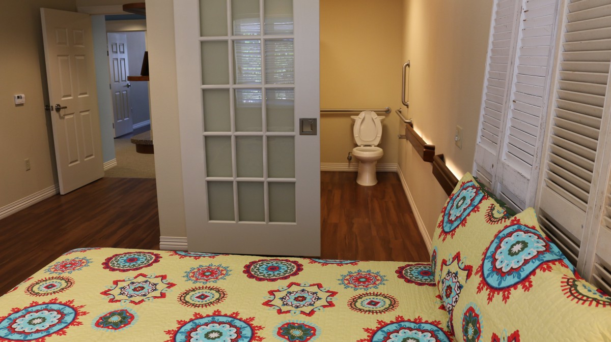 A bedroom with a colorful patterned bedspread and an adjacent accessible bathroom featuring a sliding door.