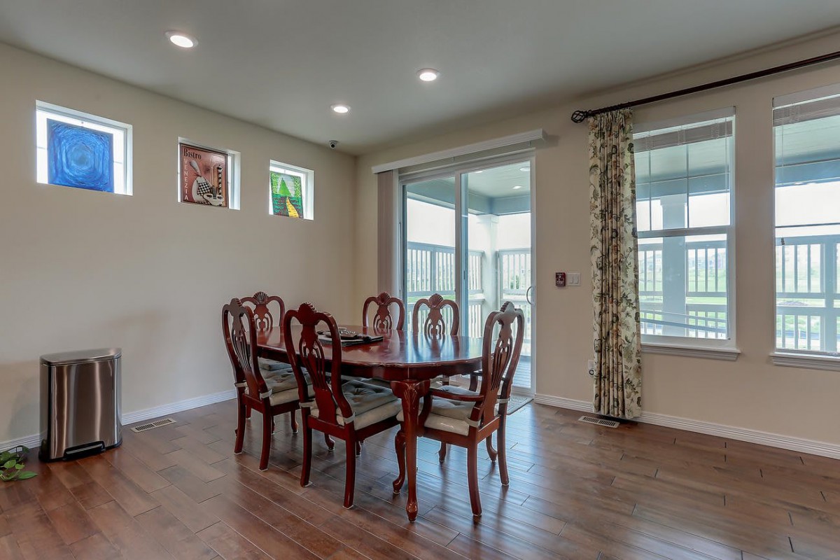 A dining room with a wooden table and chairs, featuring large windows and hardwood flooring.