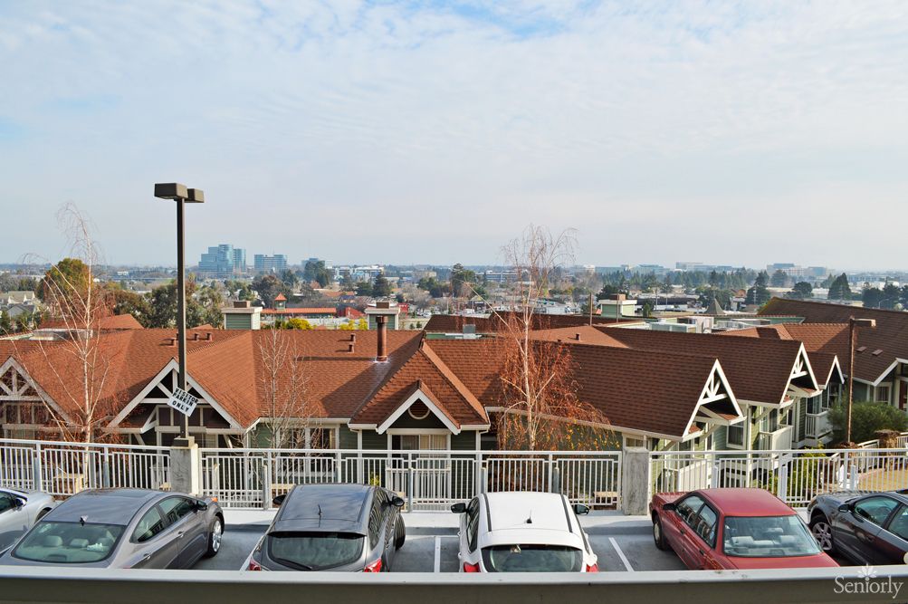 A view of a parking lot with several cars, rooftops of nearby buildings, and a distant city skyline.