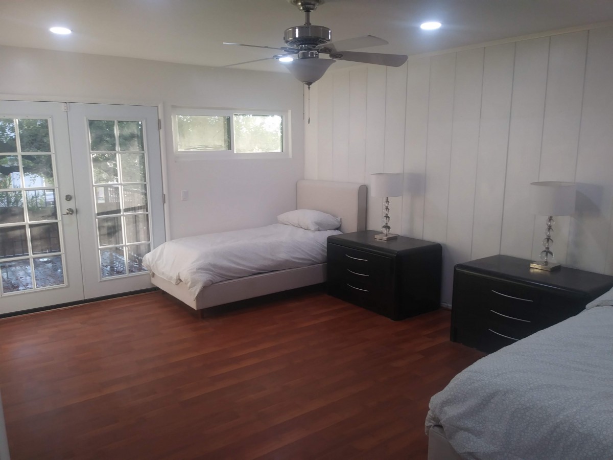 A minimalist bedroom with two twin beds, wooden floors, and a ceiling fan.