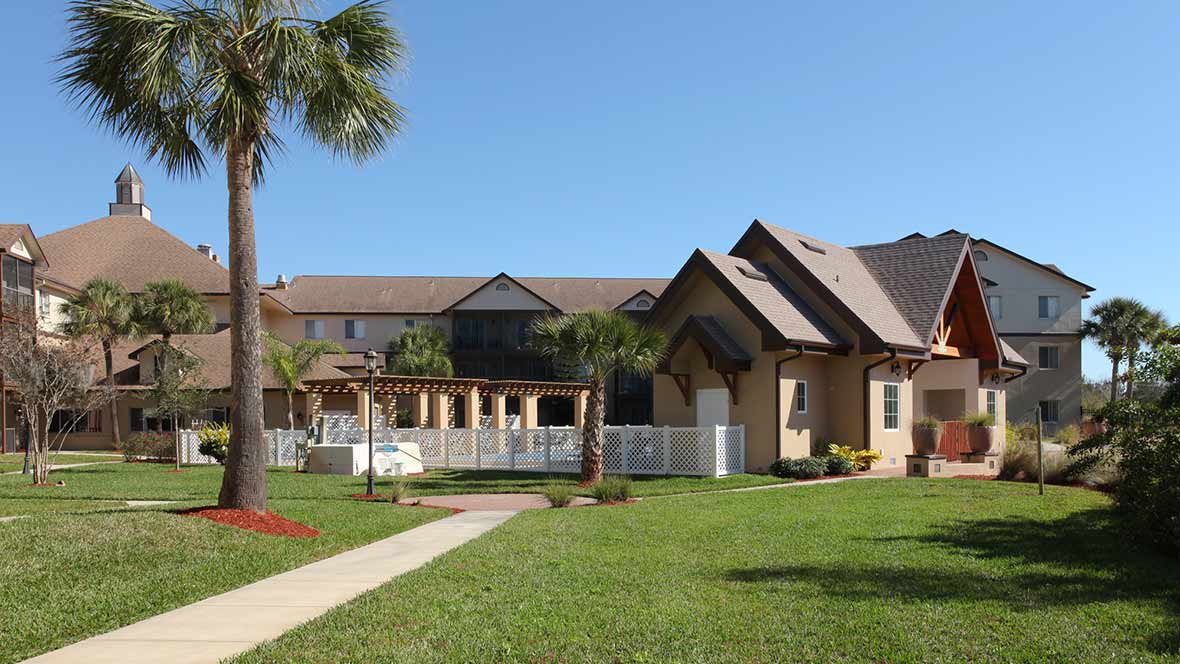 A large residential house with a well-maintained lawn and palm trees under a clear blue sky.