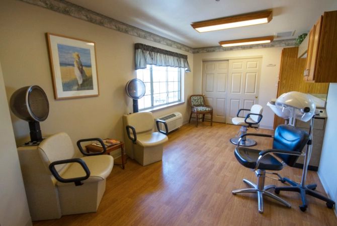 An empty waiting room in a hair salon with several chairs and natural light coming through a window.