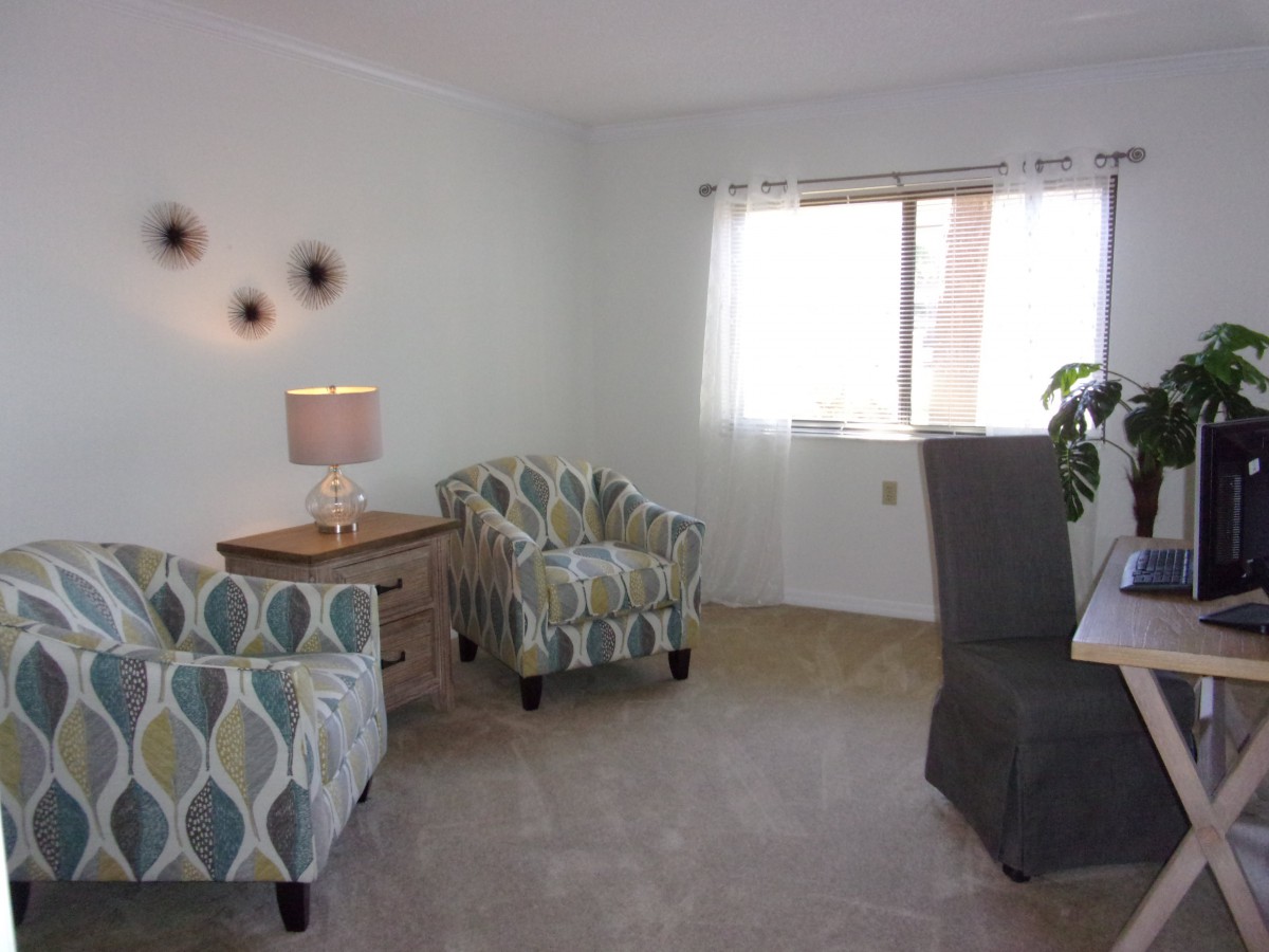 A cozy living room with patterned chairs, a side table, and a lamp near a window.