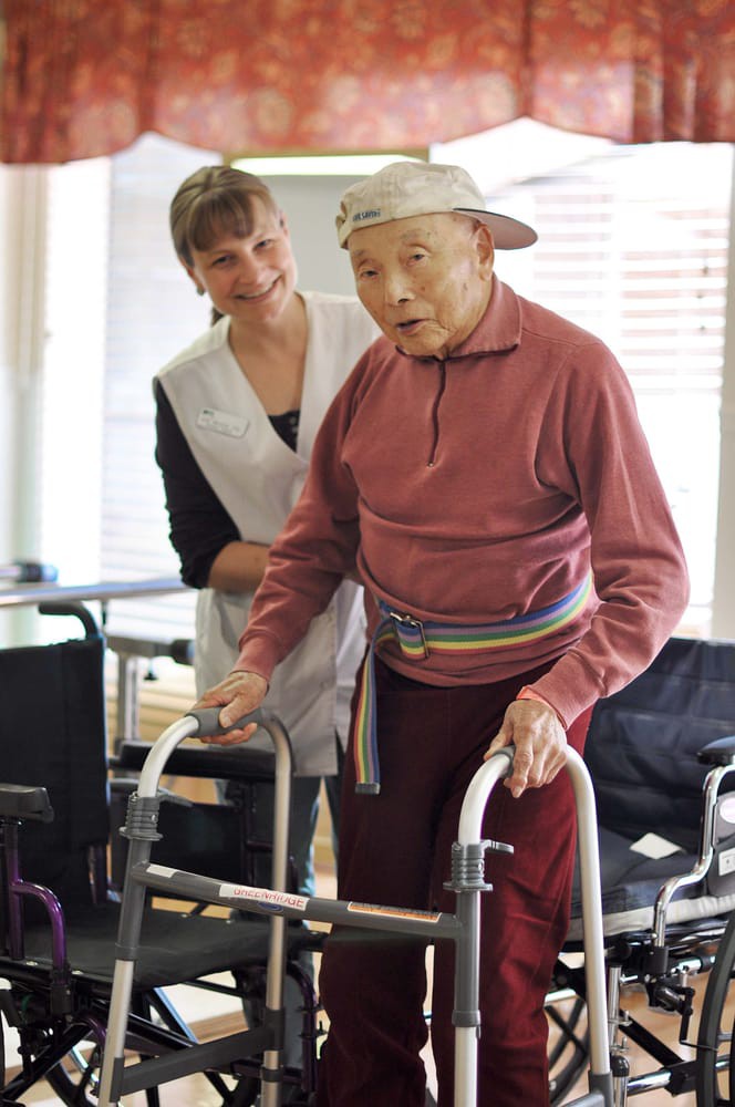 An elderly person using a walker with assistance from a caregiver during rehabilitation.