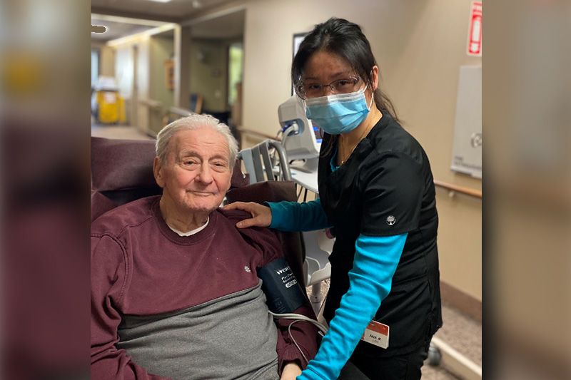 A healthcare worker wearing a mask assisting an elderly patient in a medical setting.