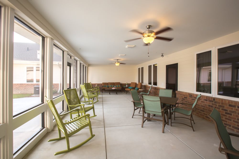 A spacious sunroom featuring rocking chairs, a dining table, and multiple windows with ceiling fans.