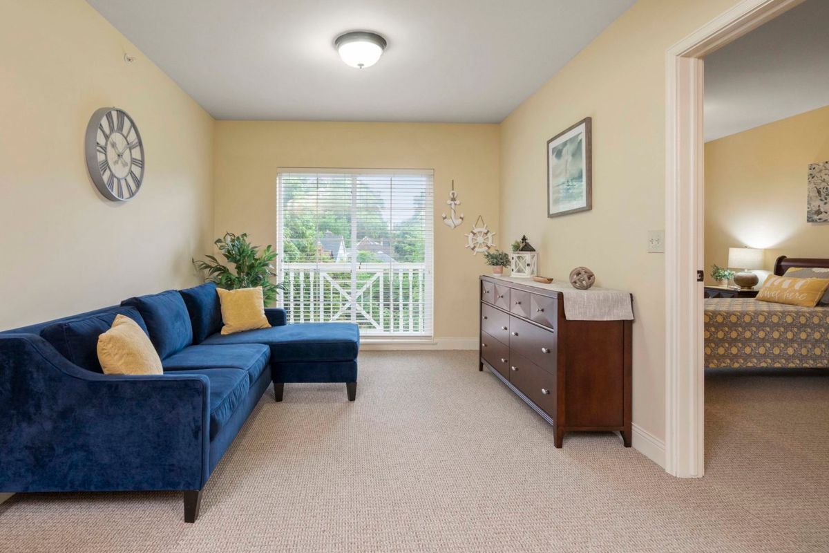 A cozy living room featuring a blue sofa with yellow pillows, a wooden sideboard, and ample natural light from the large window.