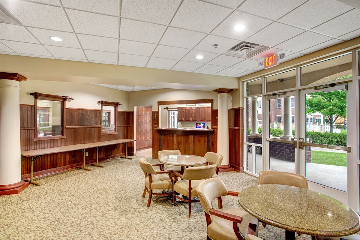 A spacious lobby area with multiple tables and chairs, featuring wood paneling and a carpeted floor.
