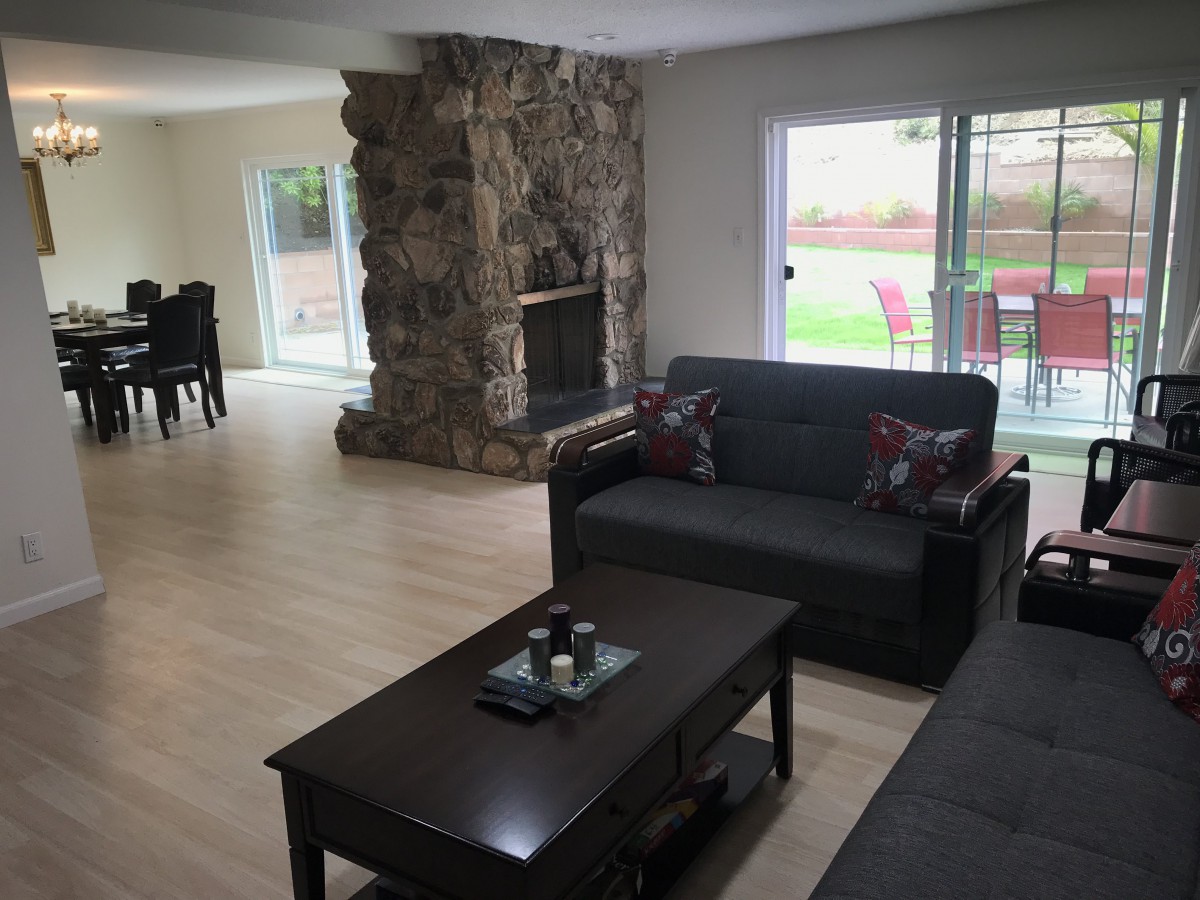 A cozy living room with a stone fireplace and modern furniture, adjacent to a dining area.