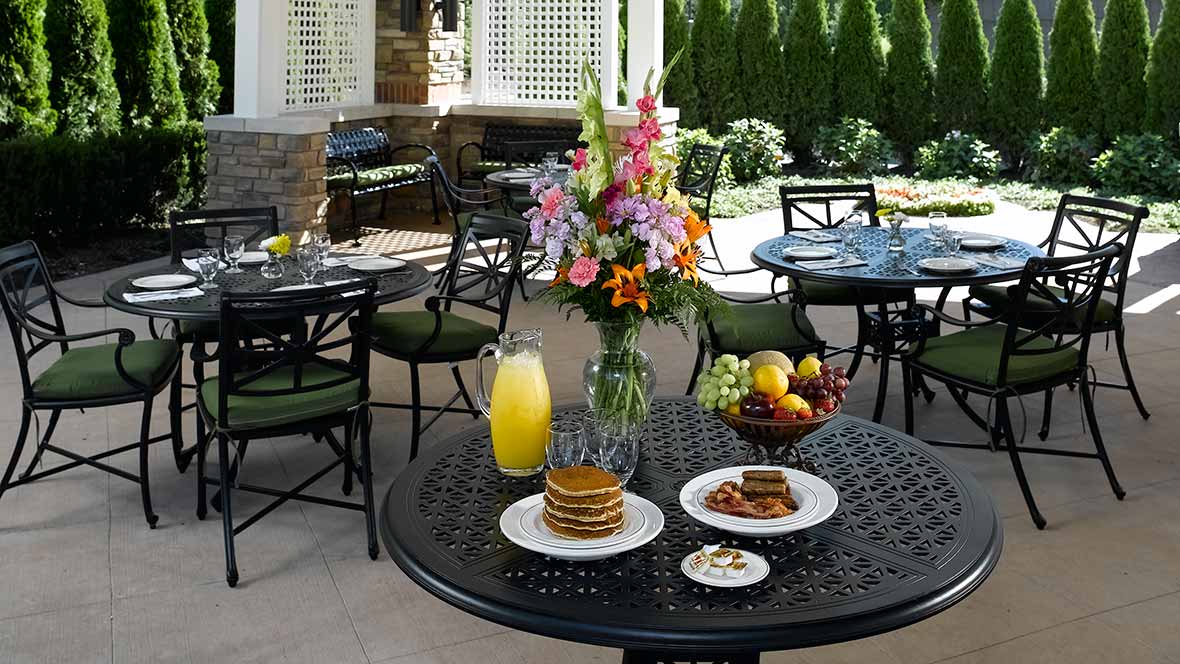 A beautifully set table on a patio with pancakes, juice, and fresh flowers.