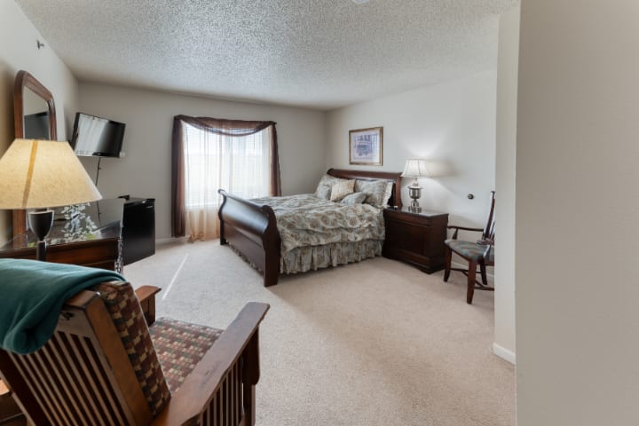 A cozy bedroom with a large bed, armchair, and a wall-mounted television.