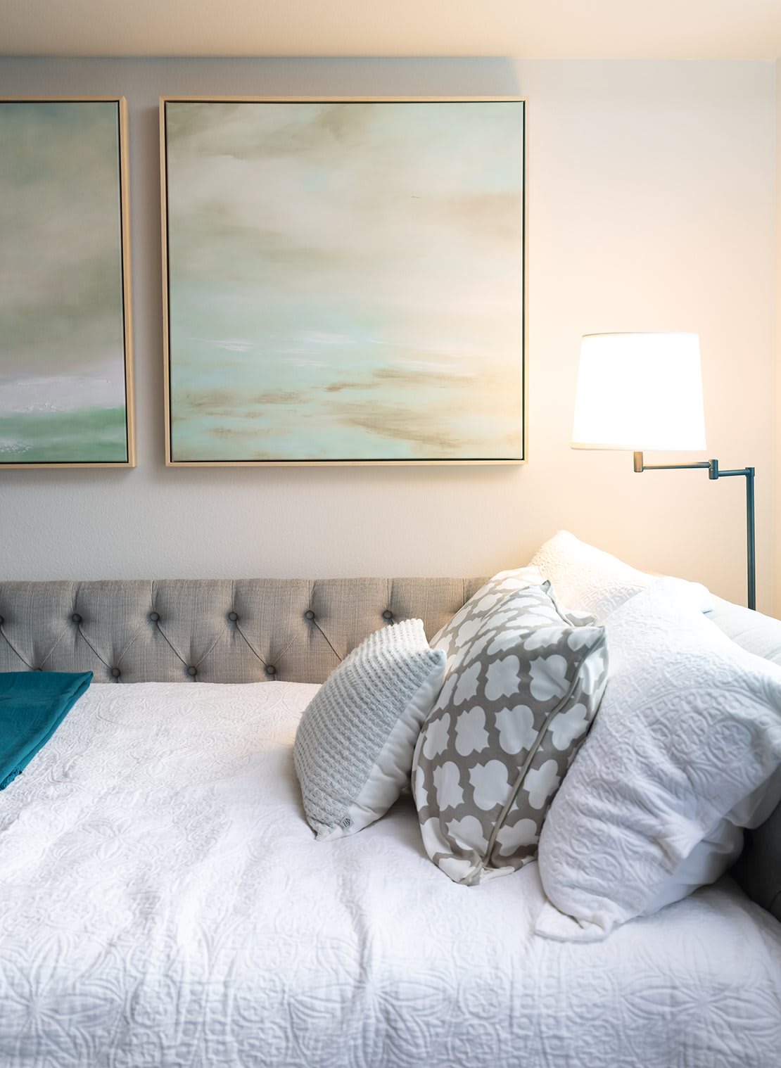 A cozy bedroom setup featuring a tufted headboard, decorative pillows, and calming artwork.