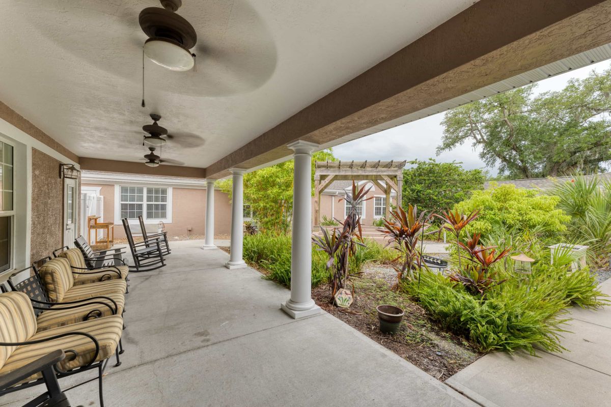 A cozy patio with rocking chairs and ceiling fans overlooking a lush garden.