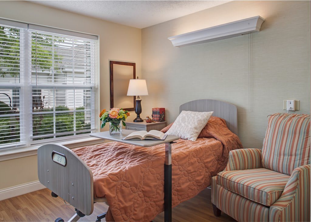 A cozy hospital room featuring a medical bed, an armchair, and a window letting in natural light.