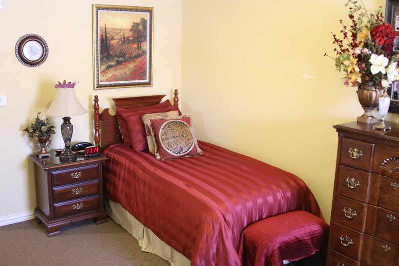A cozy bedroom with a single bed featuring red bedding and a nightstand with a lamp.