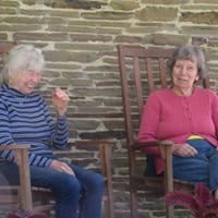 Two elderly women sitting on rocking chairs outdoors.