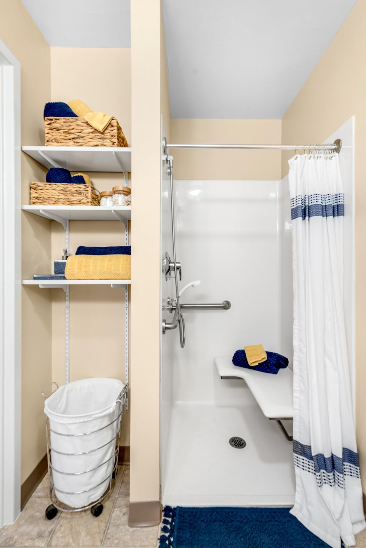 An accessible bathroom with a shower, featuring storage shelves with towels and baskets.