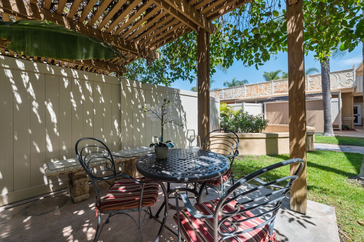 A cozy outdoor patio with a pergola providing shade over a set of table and chairs in a garden setting.