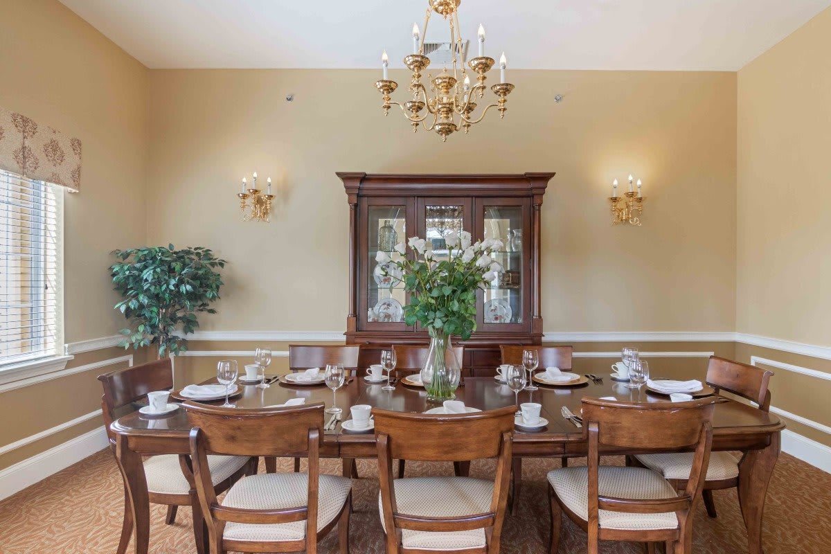 A classic dining room with an elegantly set table, chandelier, and a wooden cabinet.