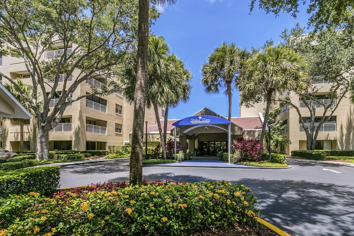 A hotel entrance surrounded by lush greenery and palm trees on a sunny day.