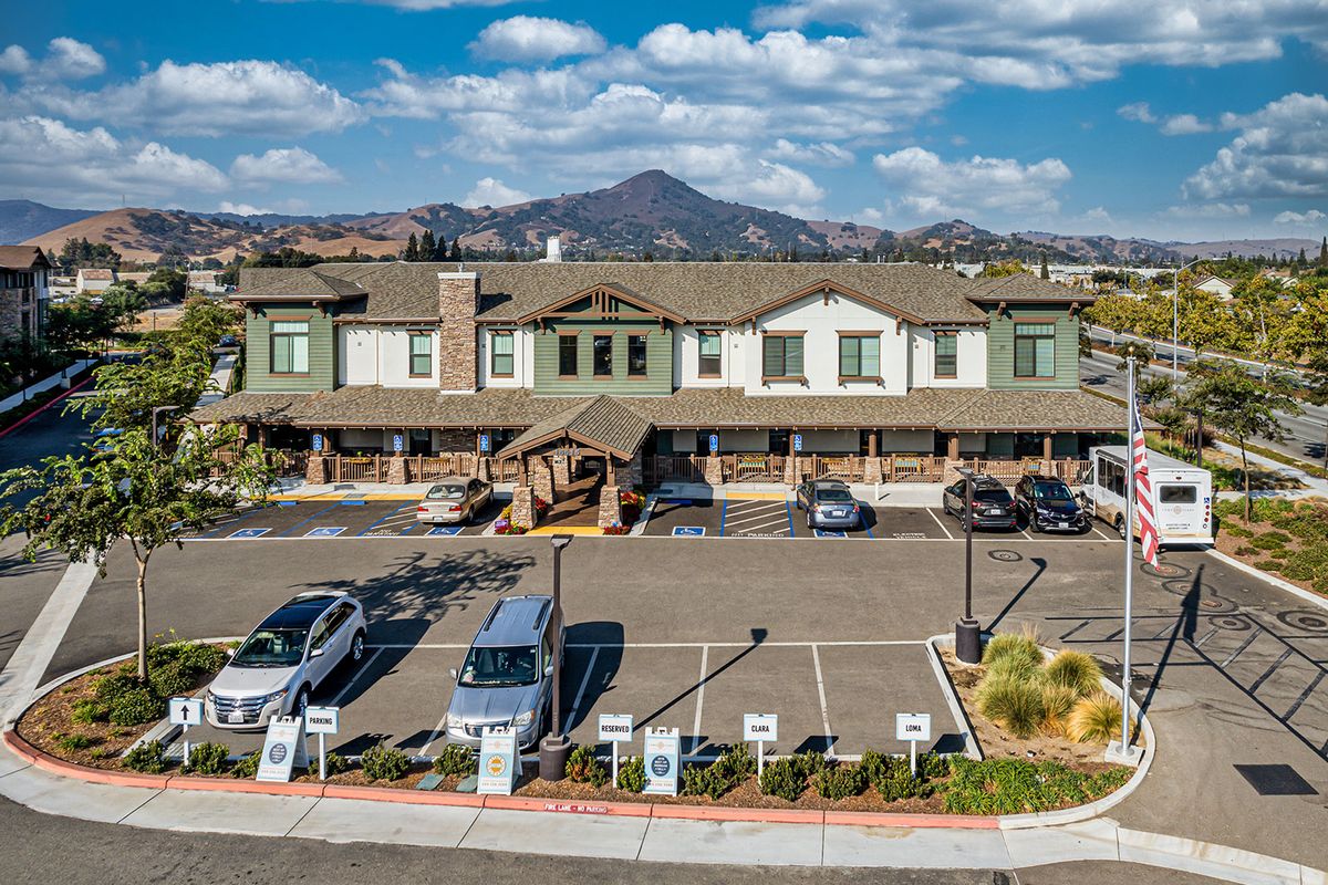 A two-story building with a parking lot in front, set against a backdrop of mountains and a cloudy sky.