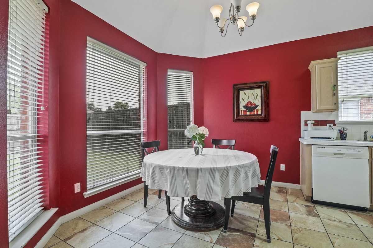 A cozy dining area with red walls and a round table set by large windows.