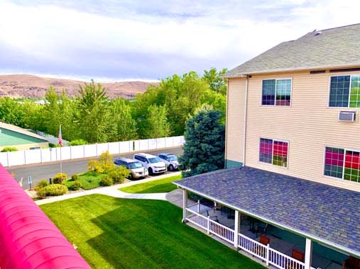 A well-maintained lawn with a building and parked cars nearby, surrounded by lush greenery.