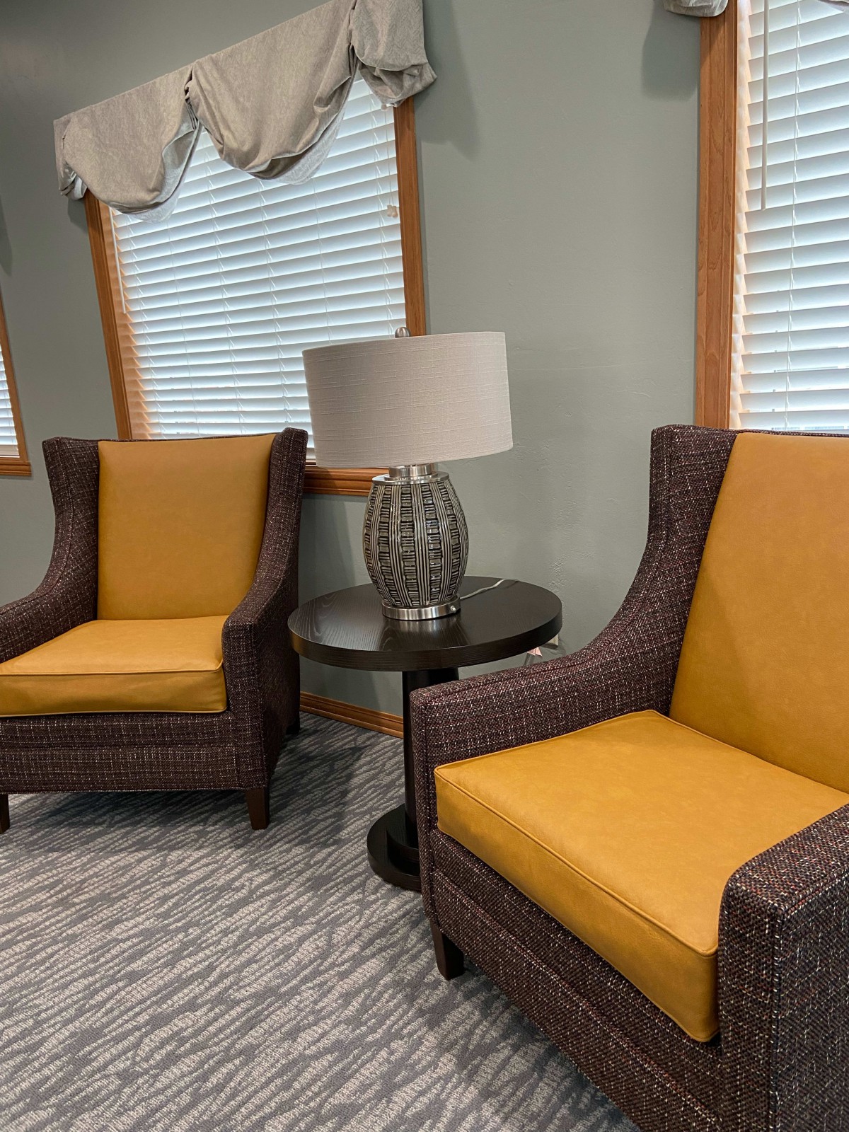 A cozy corner with two yellow and brown armchairs, a round table, and a decorative lamp in a modern living room.