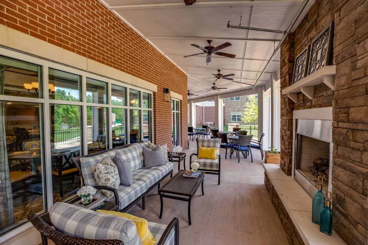 A cozy outdoor patio with comfortable seating, ceiling fans, and a fireplace.