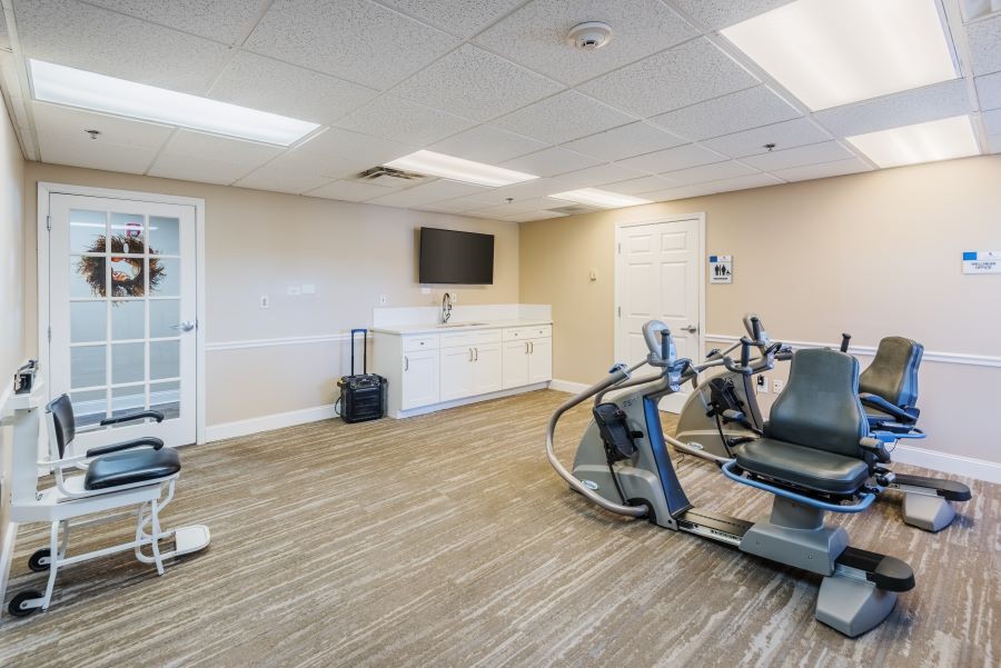 A modern gym room featuring workout equipment including an exercise bike and treadmill, with a television mounted on the wall.