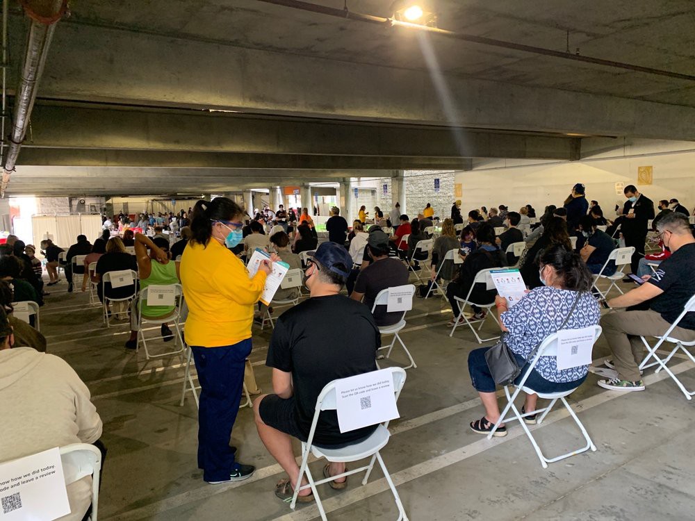 A large group of people seated in a vaccination clinic waiting area.