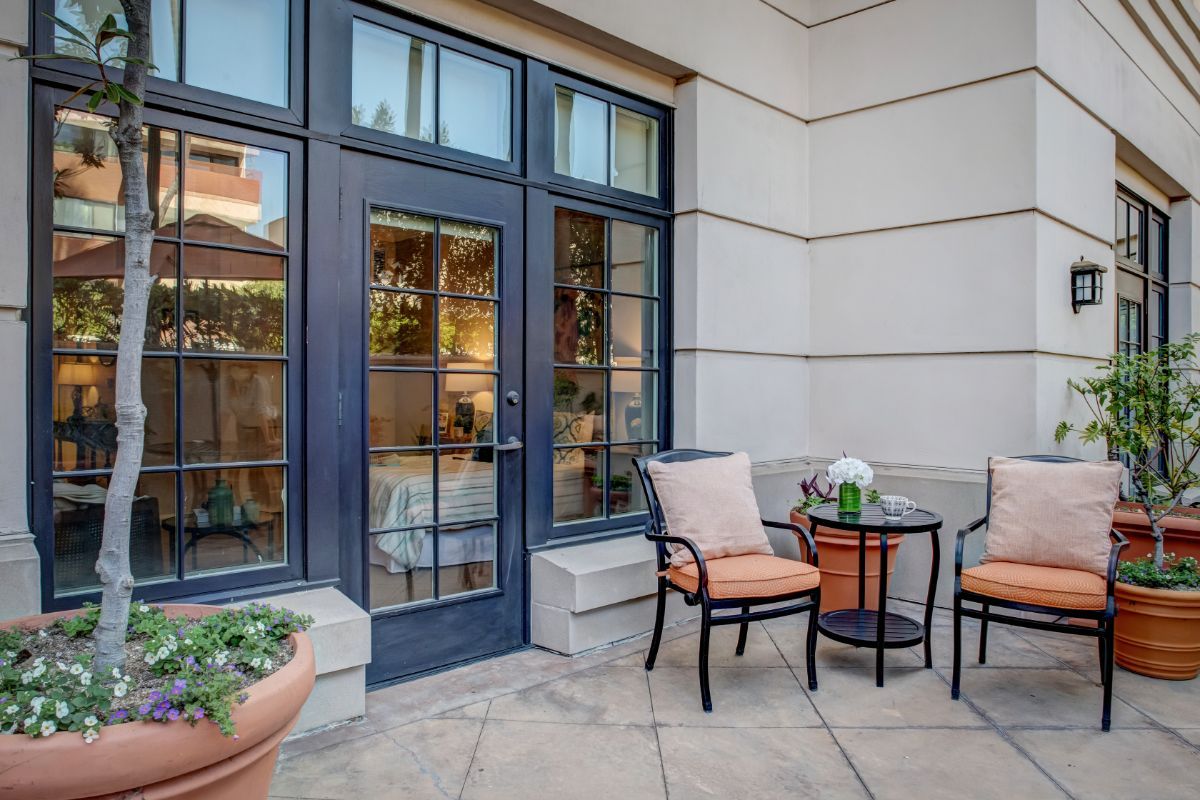 A cozy outdoor patio area with chairs and a small table, surrounded by potted plants.