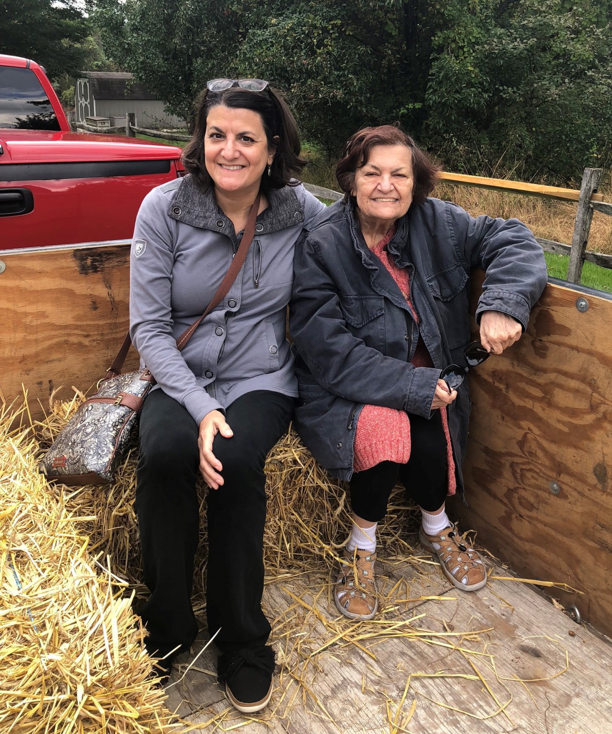 Two women sitting on hay in an outdoor setting.