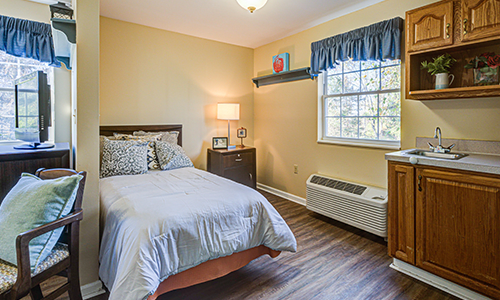 A cozy bedroom with a bed, lamp, and window providing natural light.