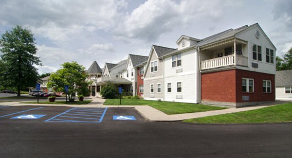 A residential building with a parking lot, featuring accessible parking spaces and a cloudy sky overhead.